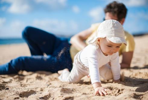 Baby protected from sun crawling on beach